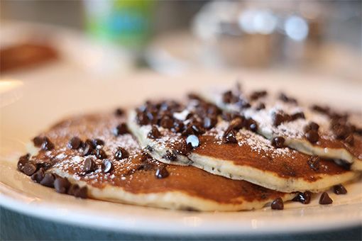Pancakes on a white plate, topped with chocolate chips and powdered sugar.