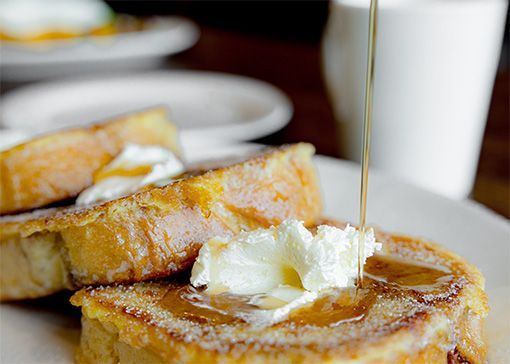 French toast with butter being drizzled with syrup on a white plate.