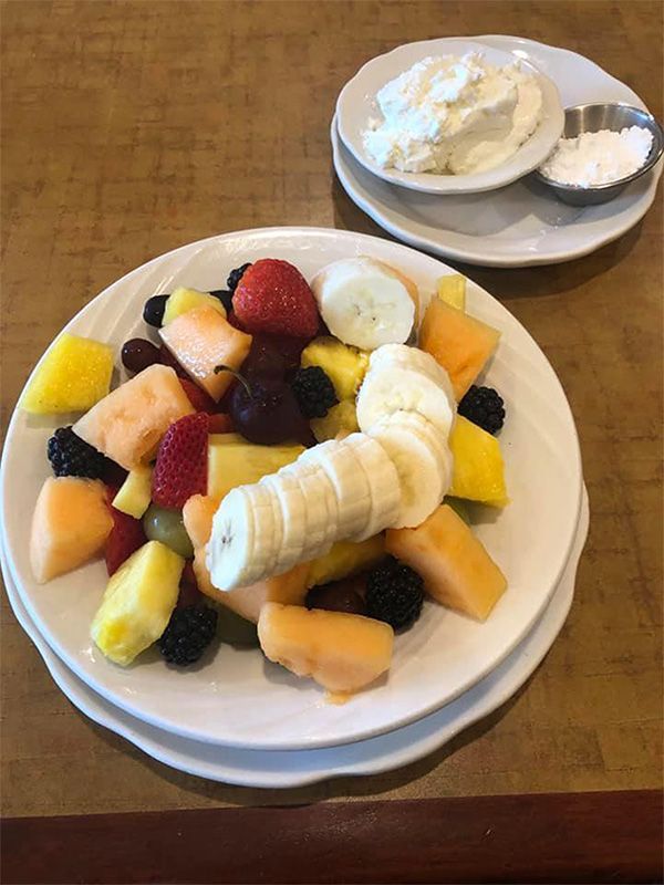Plate of fruit with whipped cream and sugar on a table. Includes cantaloupe, strawberries, banana, and blackberries.