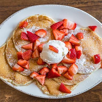 Pancakes topped with strawberries and a scoop of cream, dusted with powdered sugar, on a white plate.