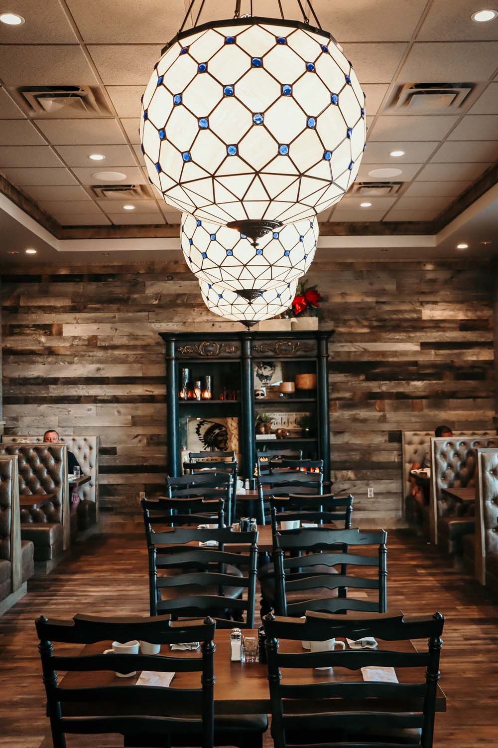 Restaurant interior with hanging globe lights, wood paneling, booths, and tables with chairs.