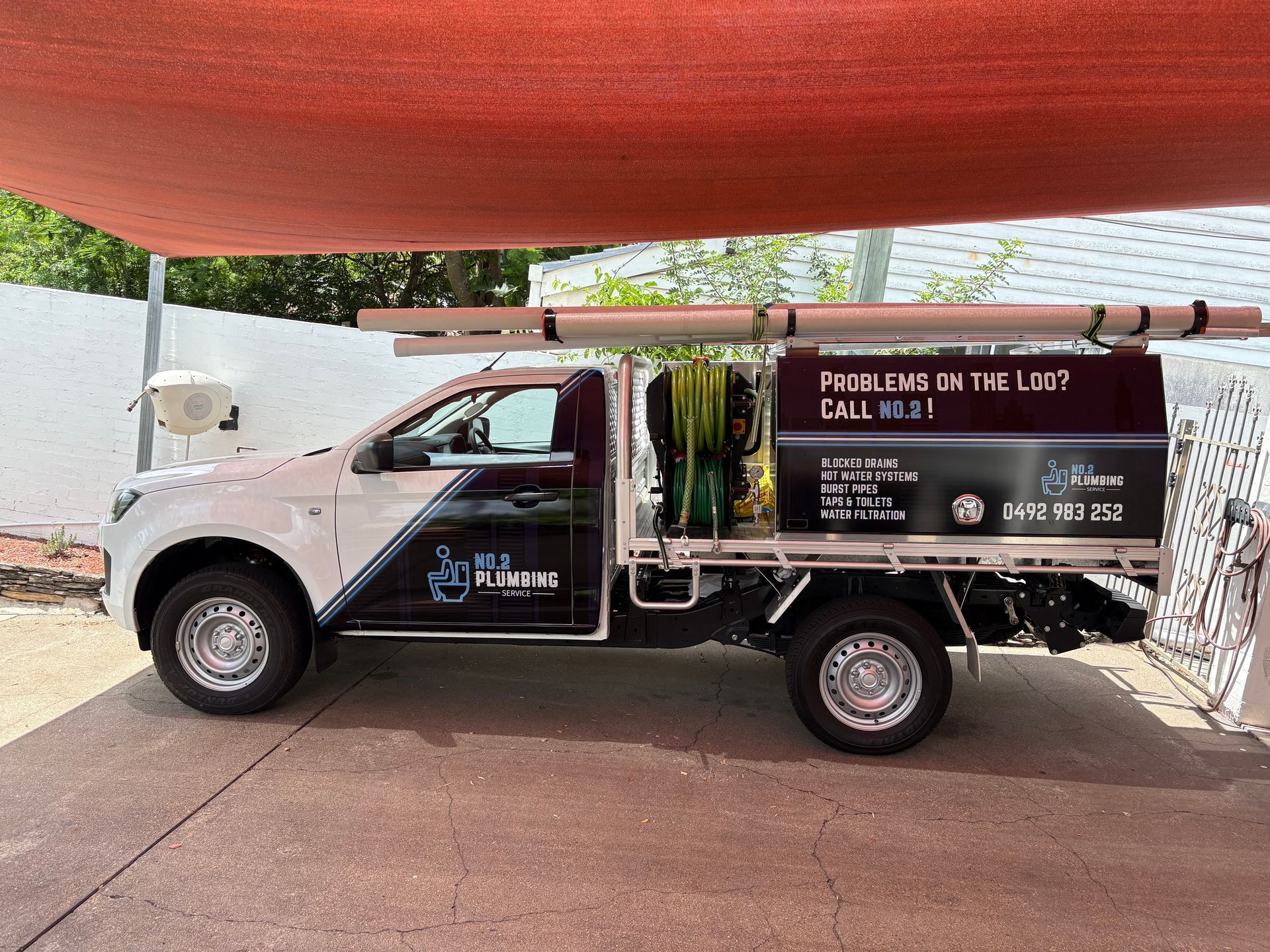 A white and black plumbing service utility truck parked outdoors under a shade sail, displaying business branding — No.2 Plumbing in Kenmore, QLD