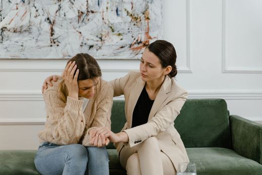 Woman comforted by another; both seated on a green sofa. Woman comforted by another; both seated on a green sofa.