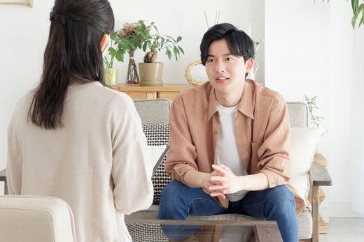 Woman facing a man sitting on a couch. They are engaged in conversation in a living room. Woman facing a man sitting on a couch. They are engaged in conversation in a living room.