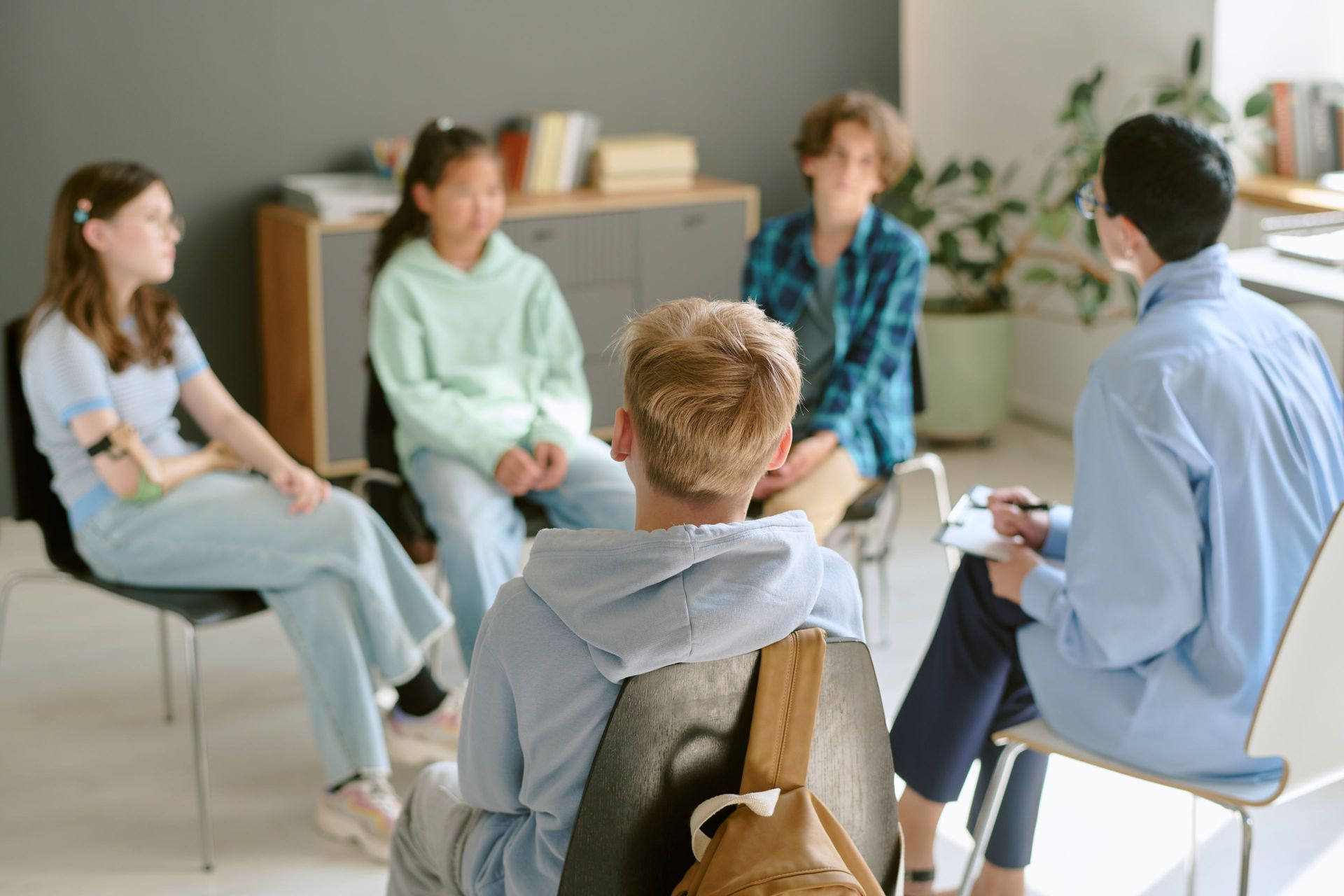 Group of teens in a circle with a person holding a clipboard, discussing in a room. Group of teens in a circle with a person holding a clipboard, discussing in a room.