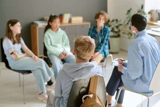 A group of teens in a circle with a counselor, discussing in an office setting. A group of teens in a circle with a counselor, discussing in an office setting.