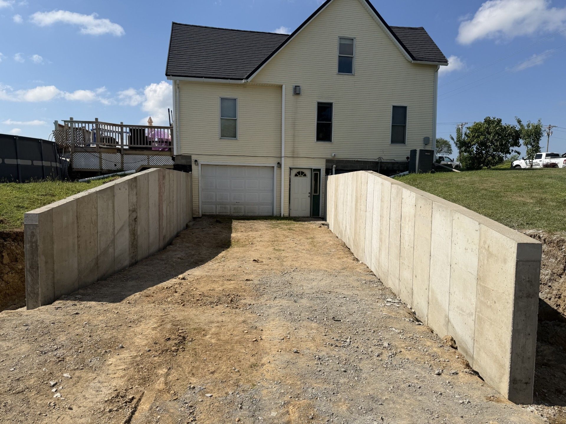 Empty gravel driveway bordered by concrete retaining walls leading to a beige house with a dark roof