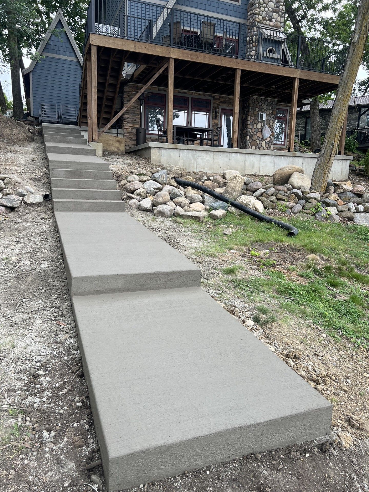 Concrete walkway and stairs leading up to a raised wooden deck beside a lakeside house.