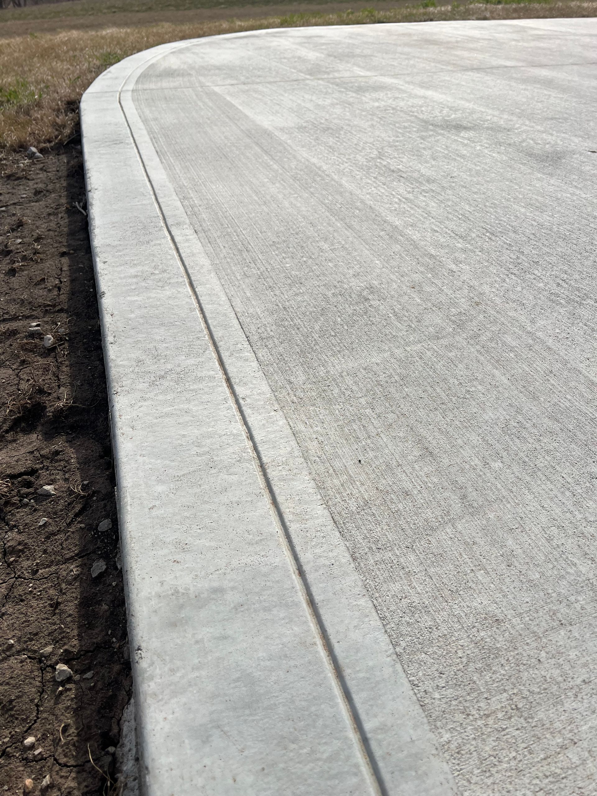 Curved concrete curb along the edge of a paved road beside bare soil