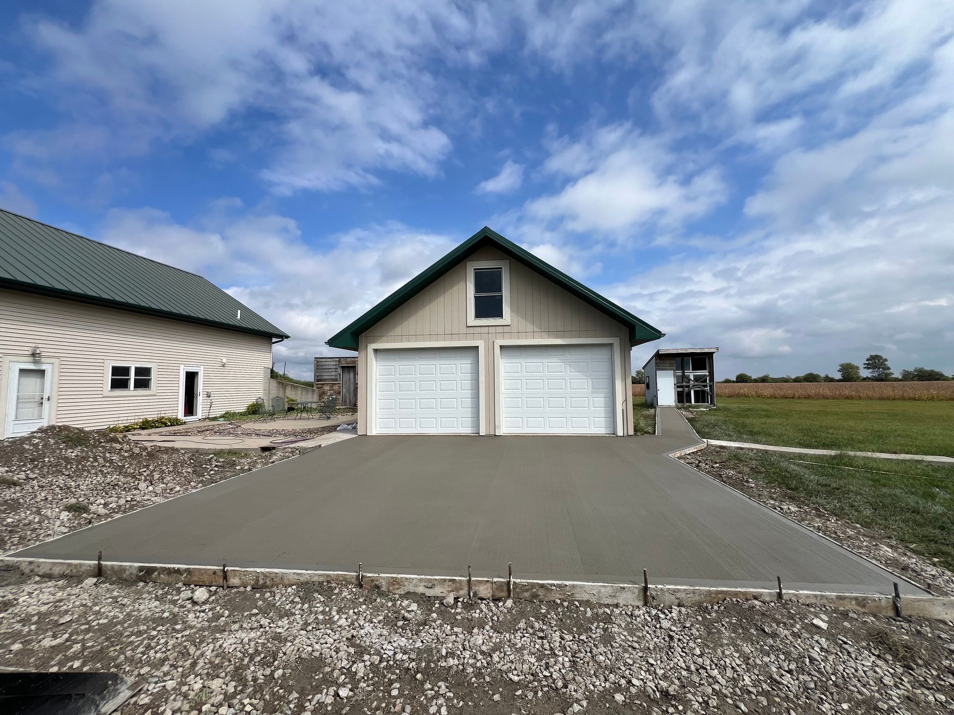 New concrete driveway leading to a white double garage under a cloudy sky