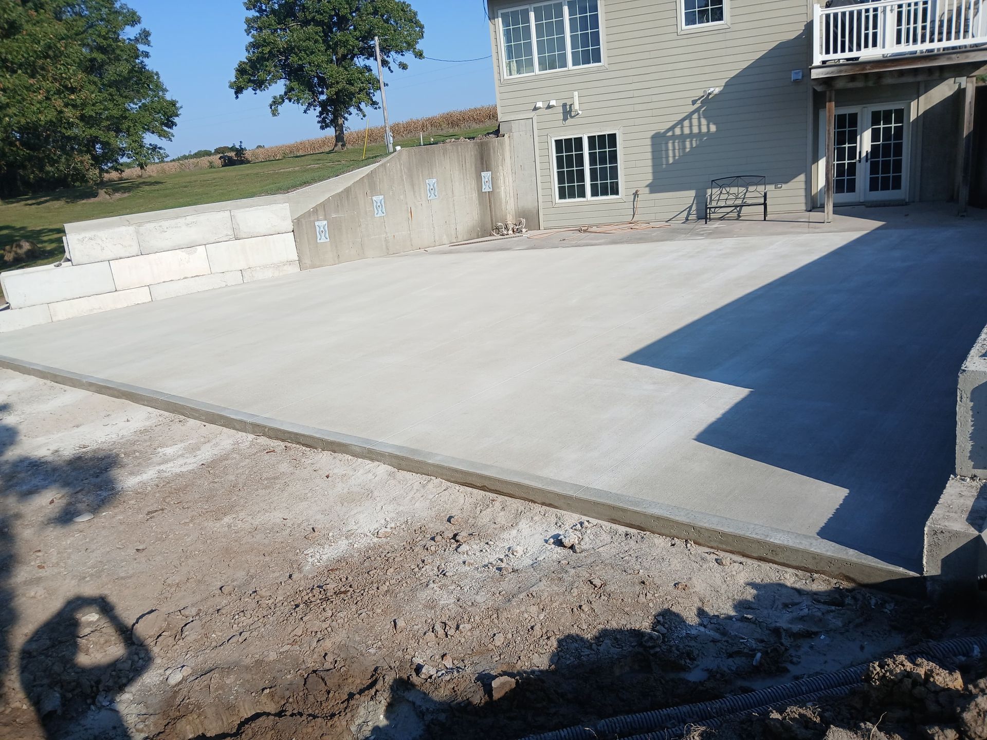 Concrete patio beside a house with a retaining wall and dirt foreground