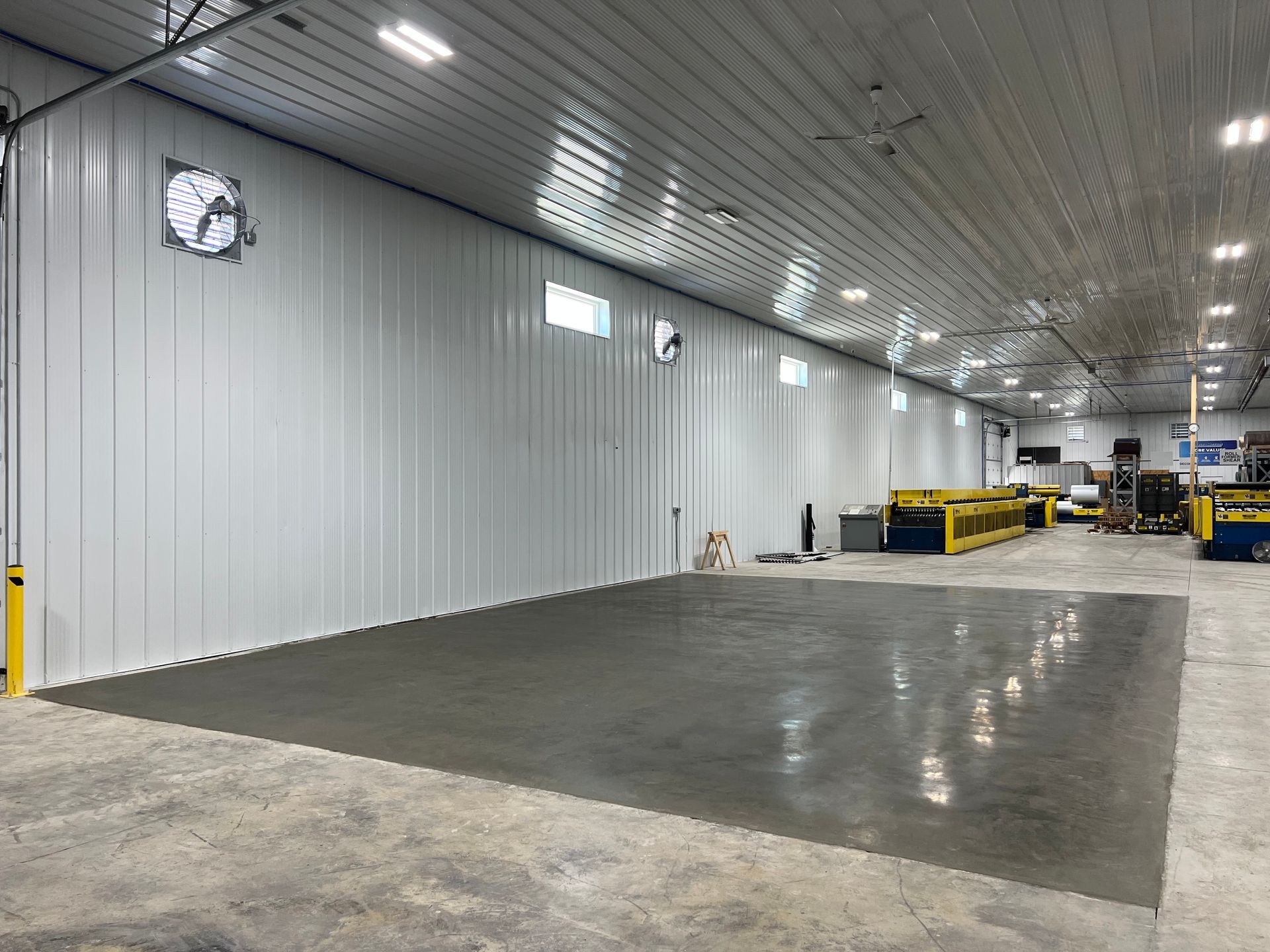 Empty industrial warehouse with gray concrete floor, white walls, and overhead lights