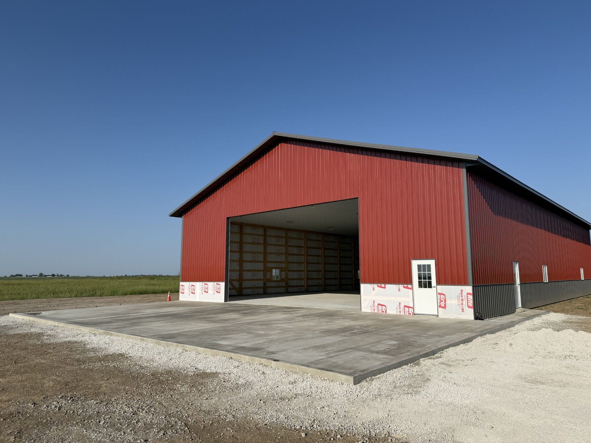 Red barn-style shed with large open doors on a gravel lot under a clear blue sky