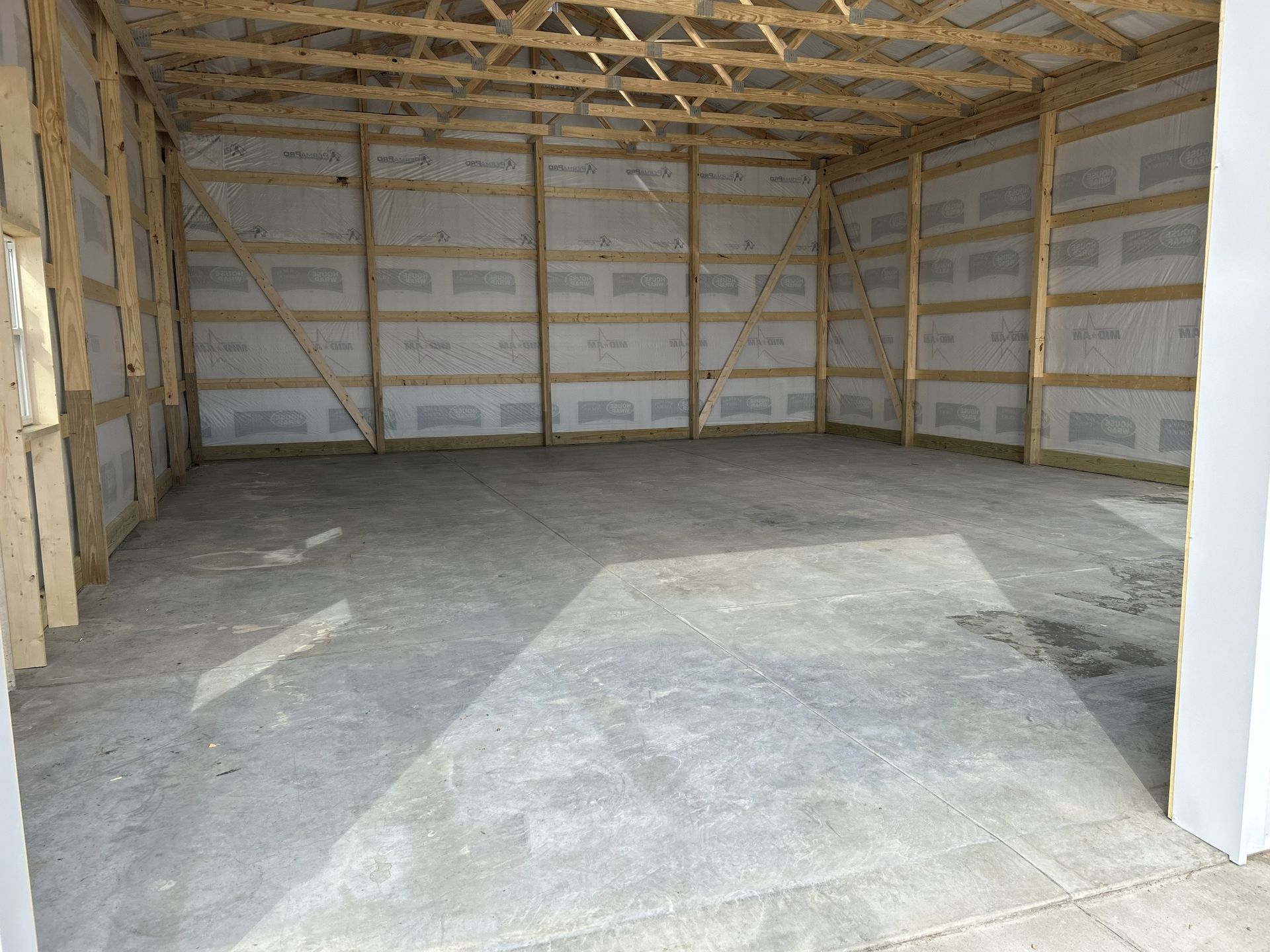 Empty unfinished garage with concrete floor, exposed wood framing, and insulation on the walls and ceiling.