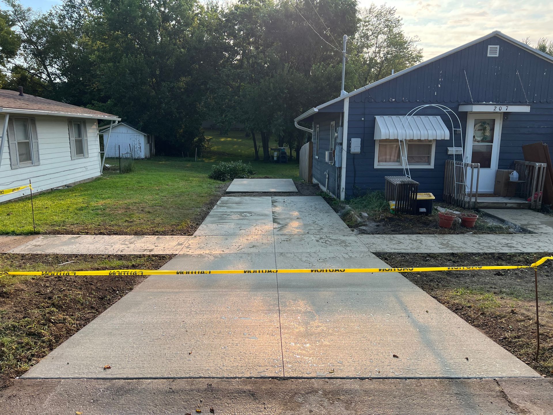 Concrete driveway beside blue house, blocked by yellow caution tape across the entrance.