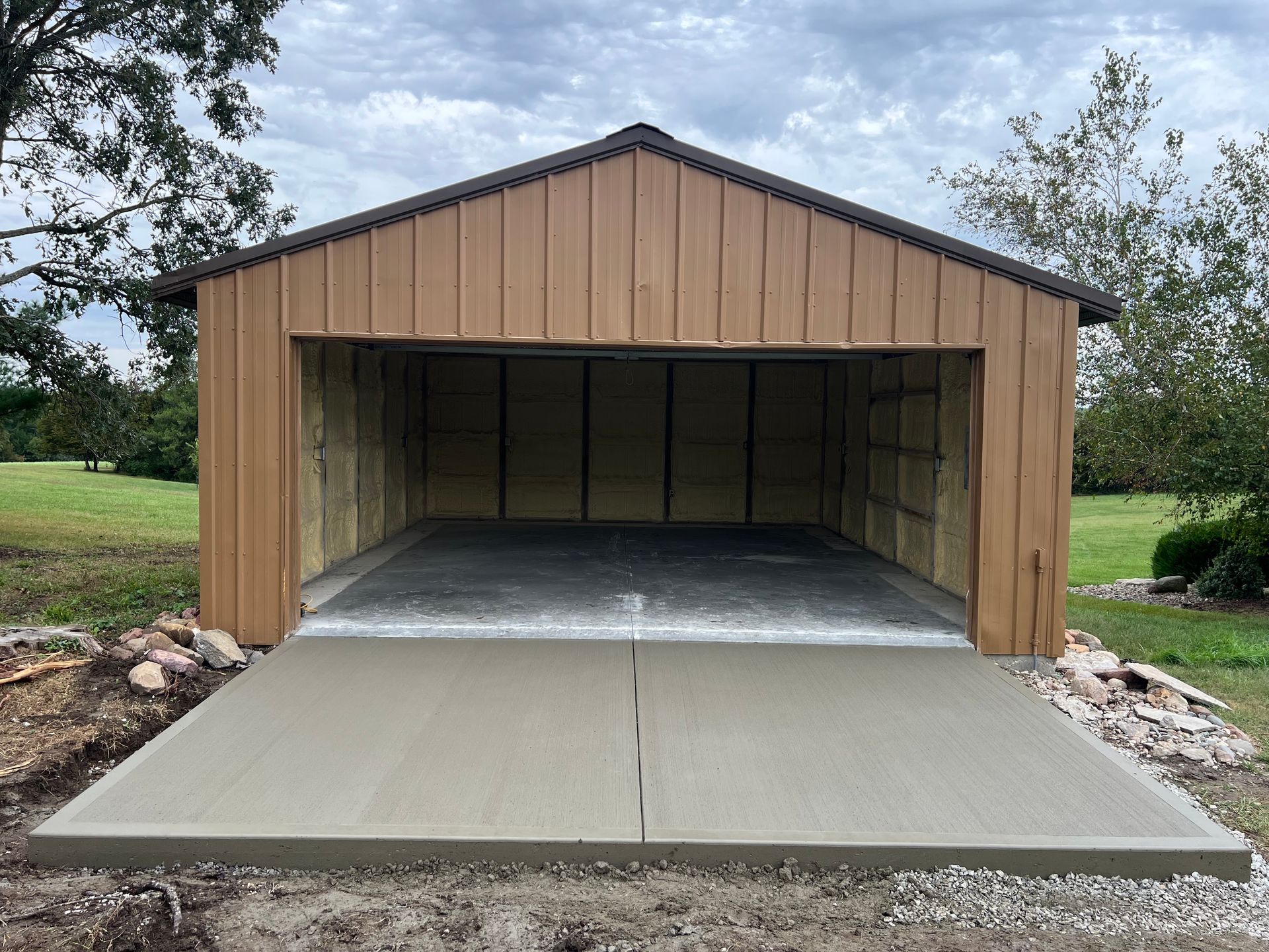 Open-front wooden garage with a concrete driveway in a rural yard