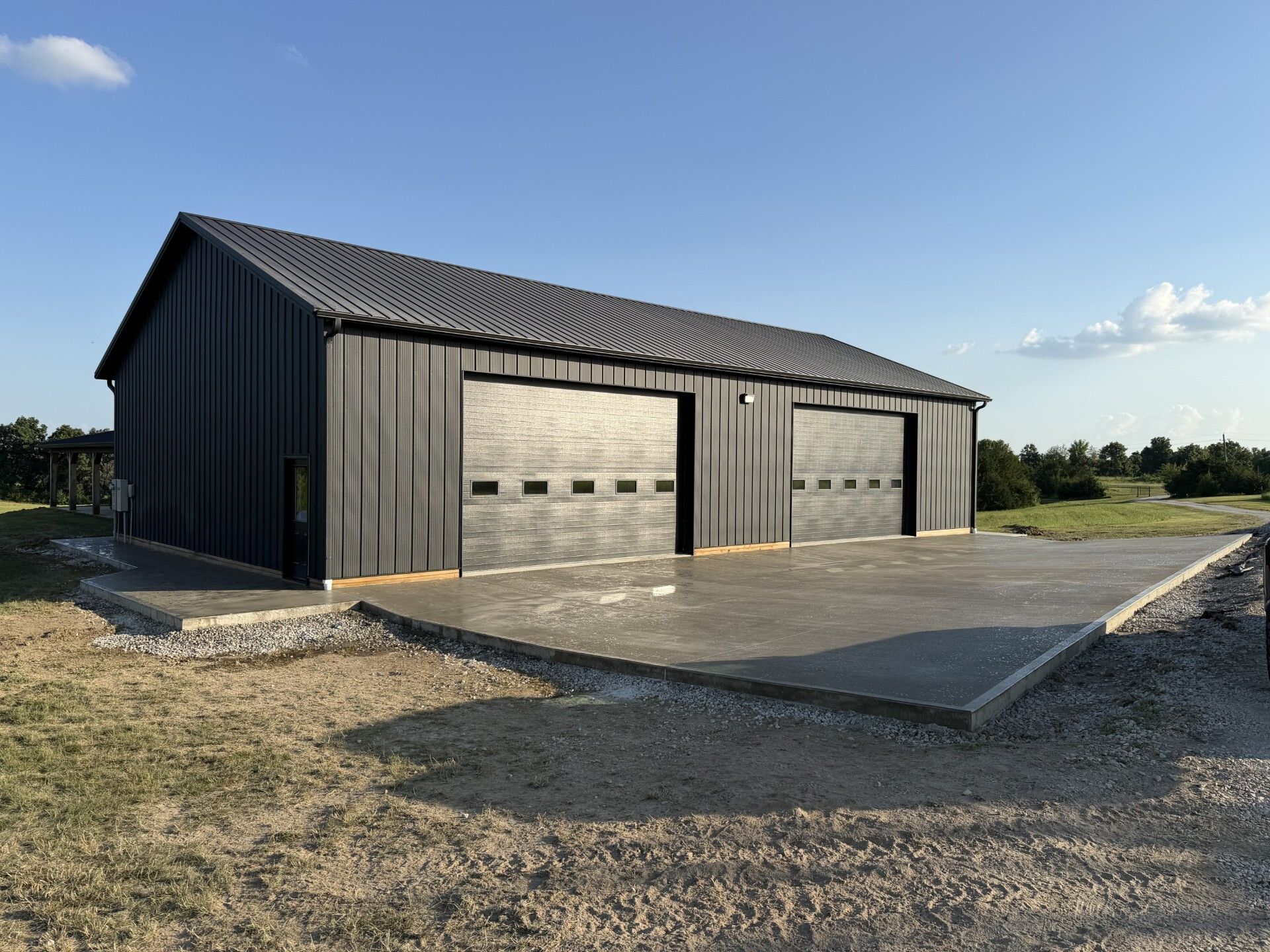 Dark metal garage with two roll-up doors beside a concrete driveway under a clear sky