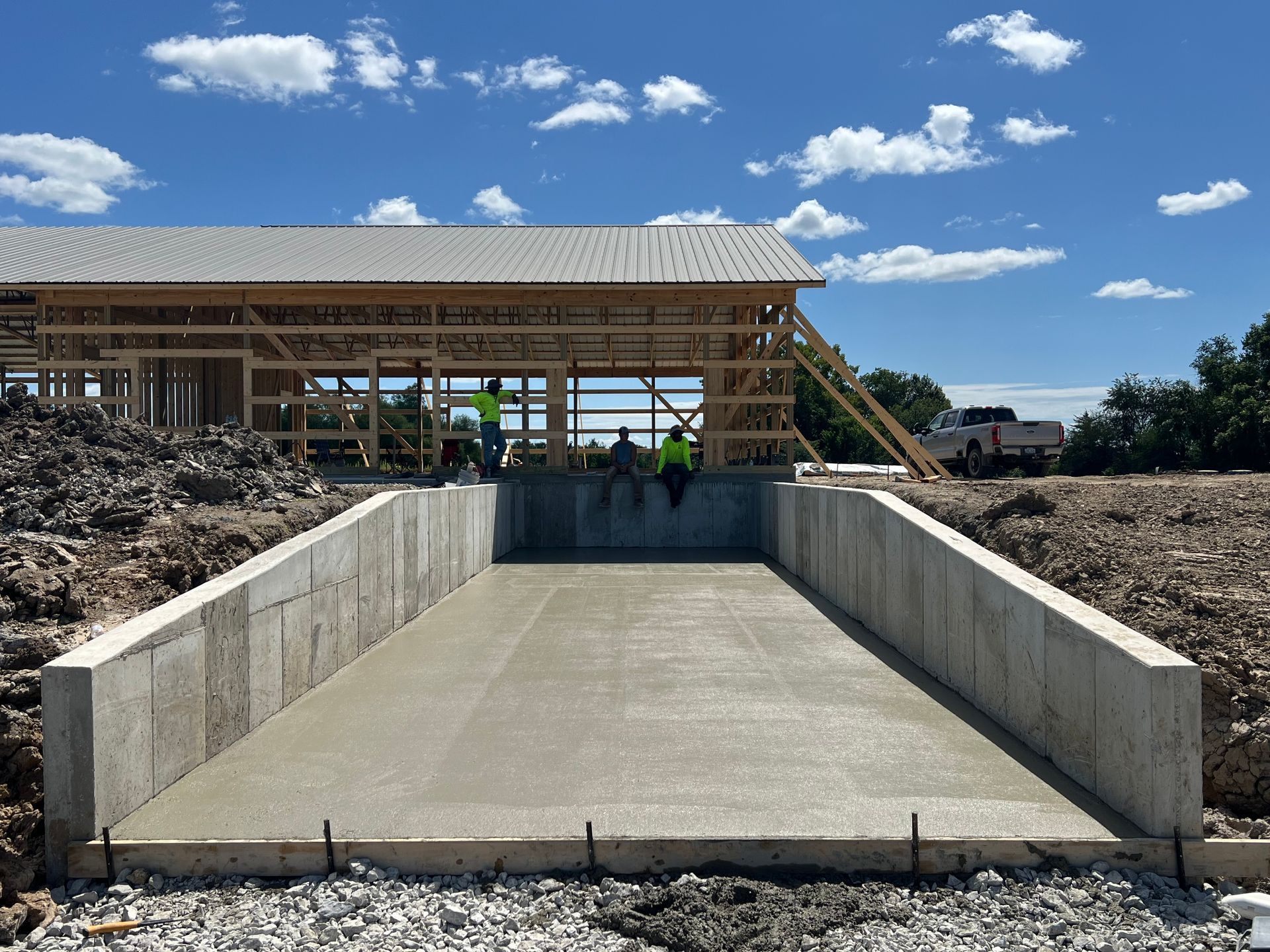 Concrete access ramp under construction beside a wooden building, with workers and blue sky overhead