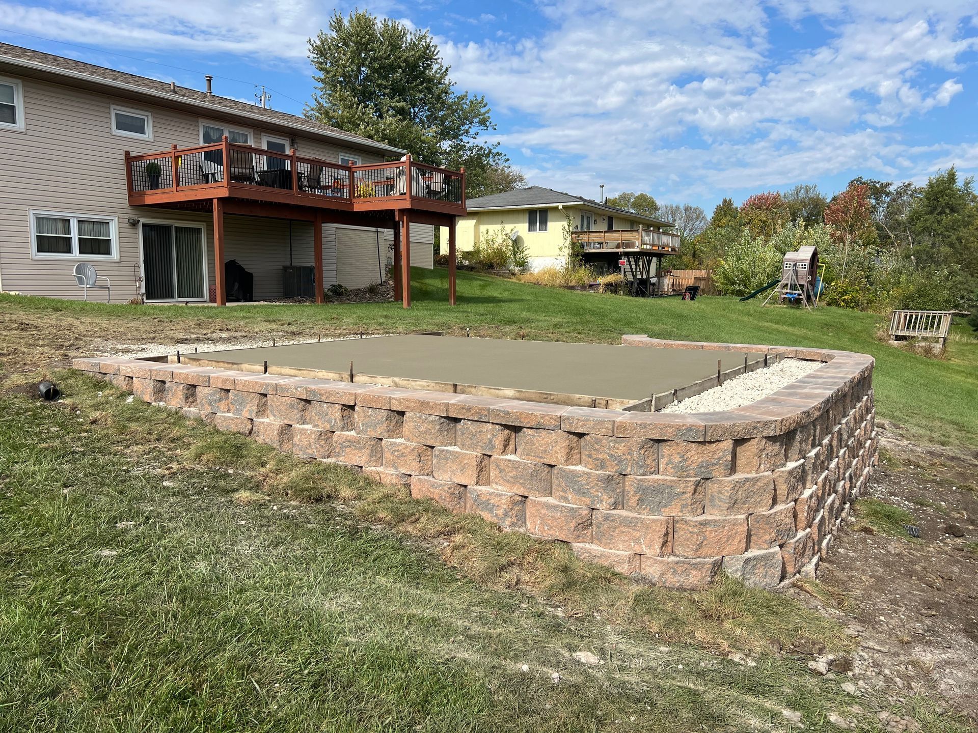 Backyard with a raised stone retaining wall around a grassy lawn beside a house deck.