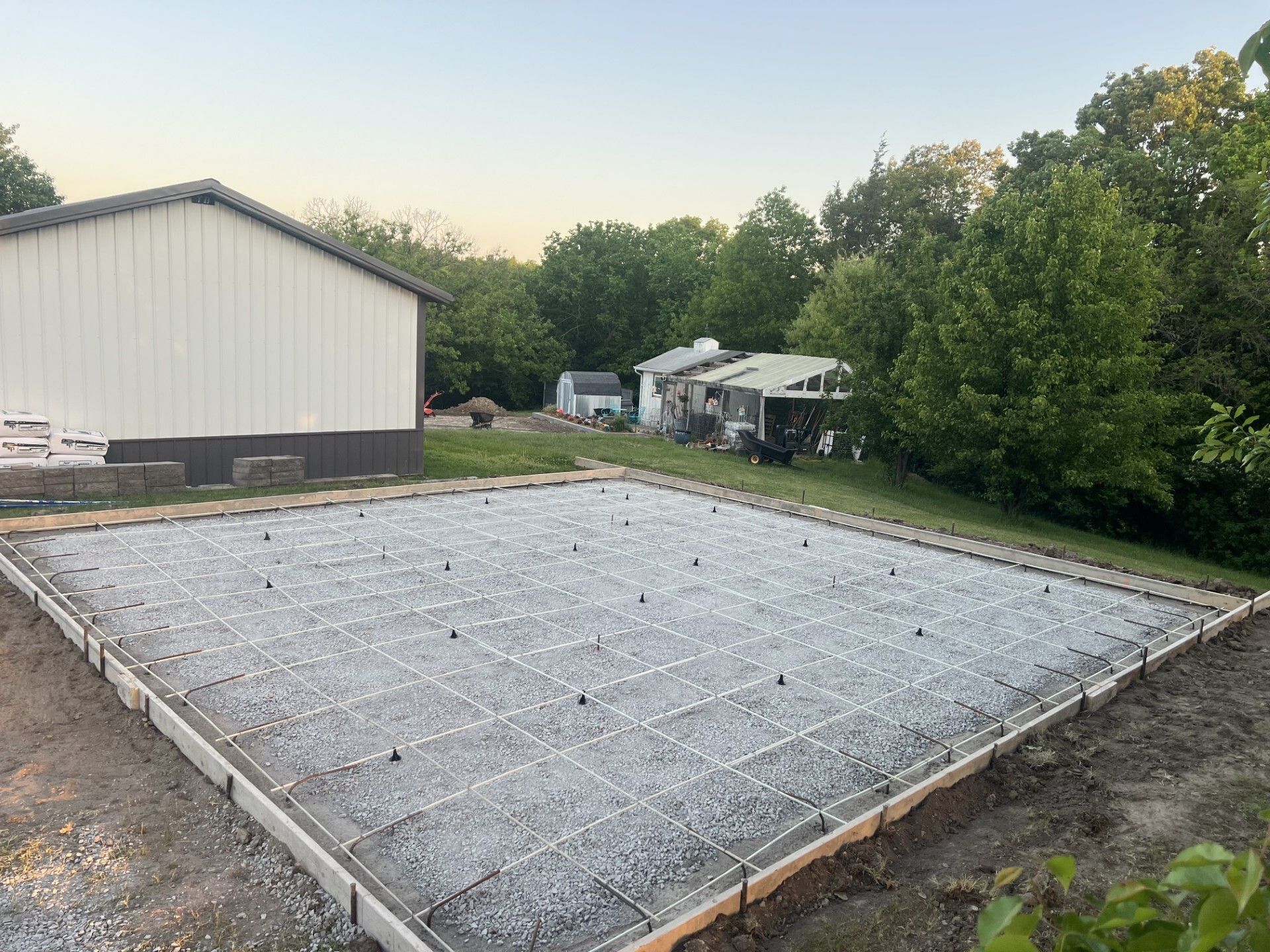 Concrete slab foundation under construction beside a white building and trees