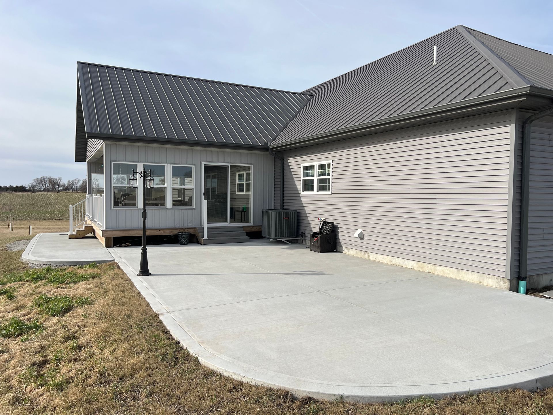 New concrete patio beside a beige house with covered porch and dark gray roof