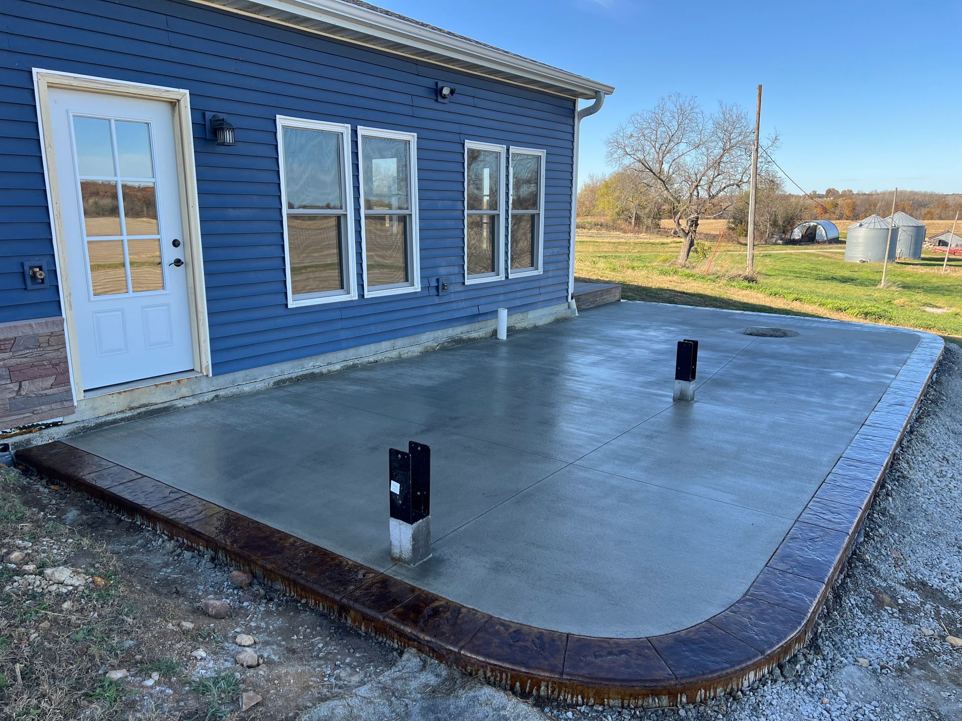 Blue house with a large concrete patio, white trim, and two black posts in a yard.