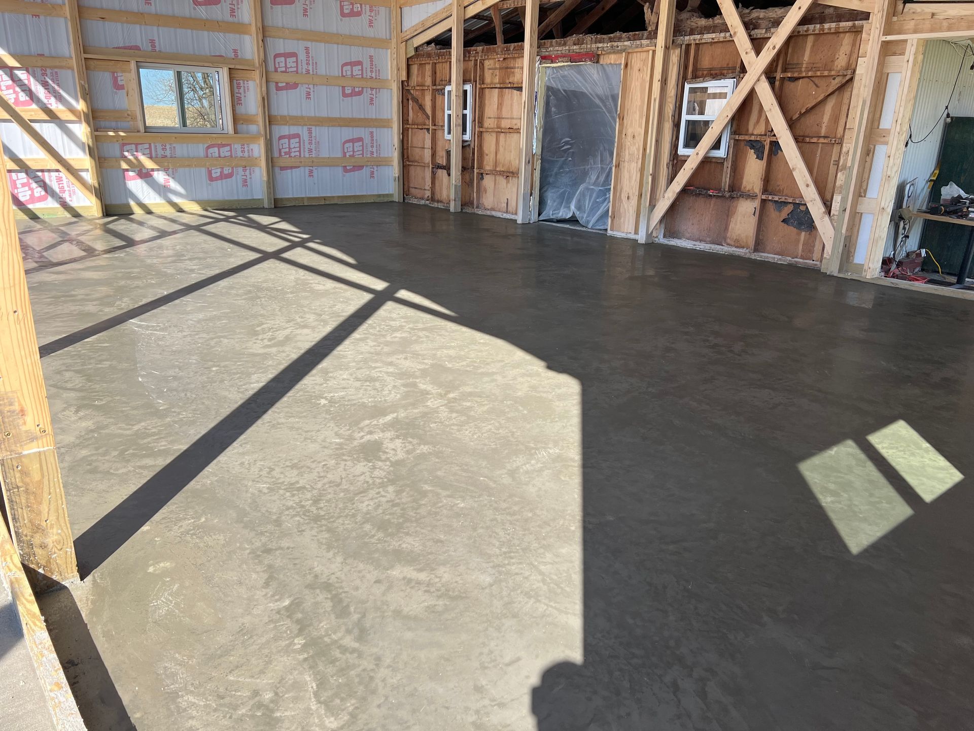 Interior of an unfinished room with a freshly poured concrete floor and exposed wall framing.