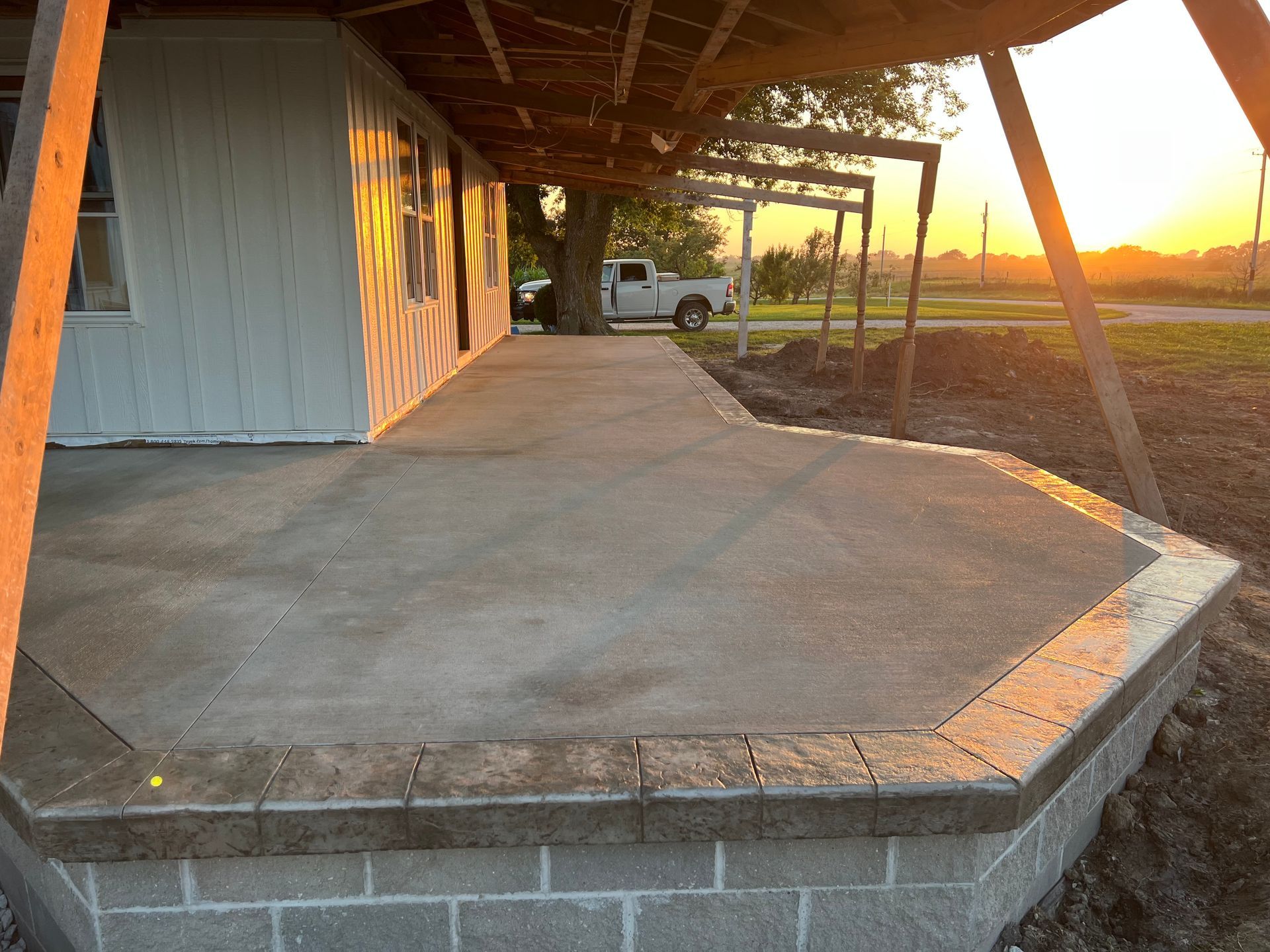 Concrete porch beside a white shed at sunset, with a gravel yard and open field beyond.