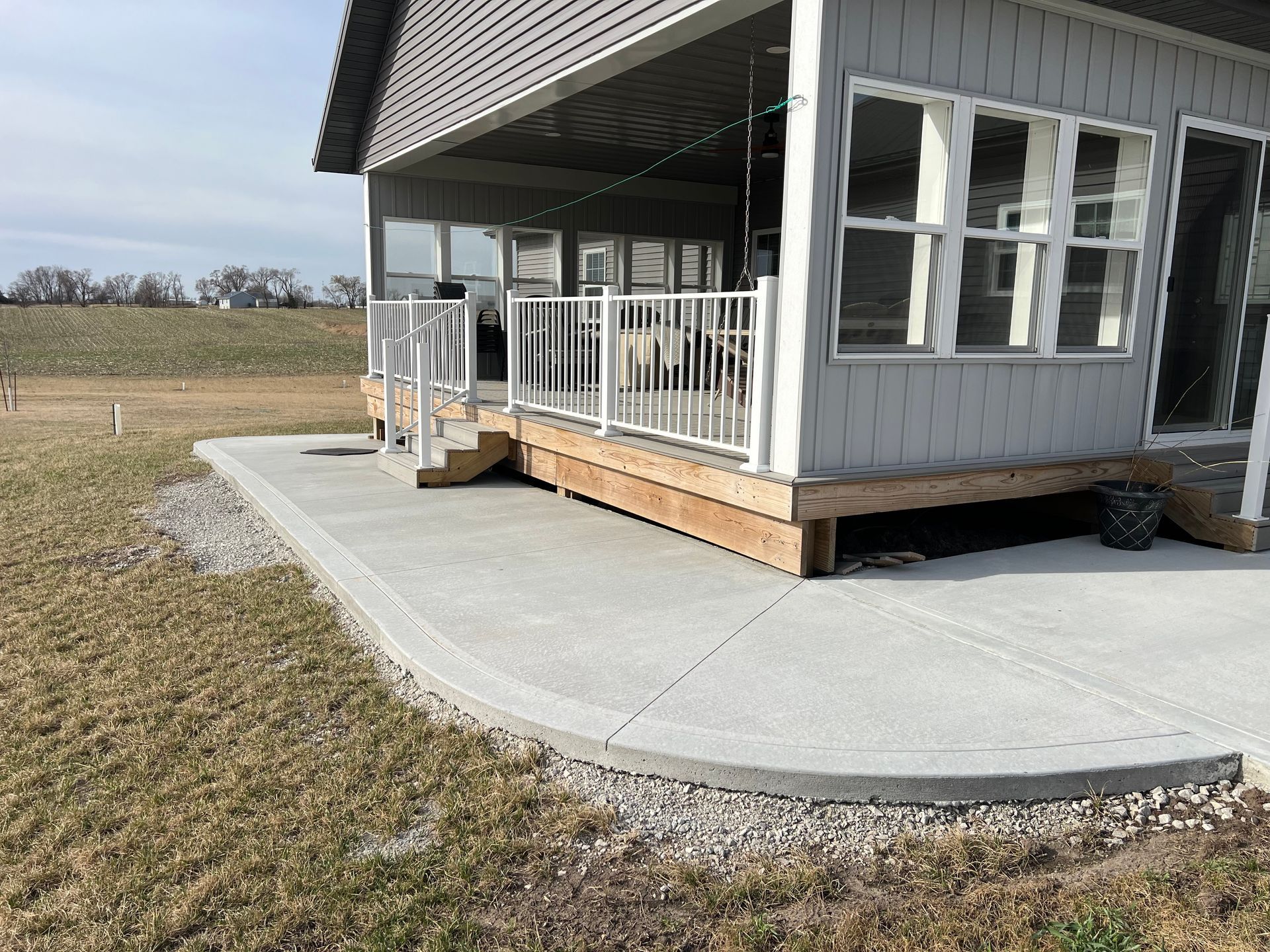 Gray house porch with white railings and a concrete ramp/walkway on a grassy lot