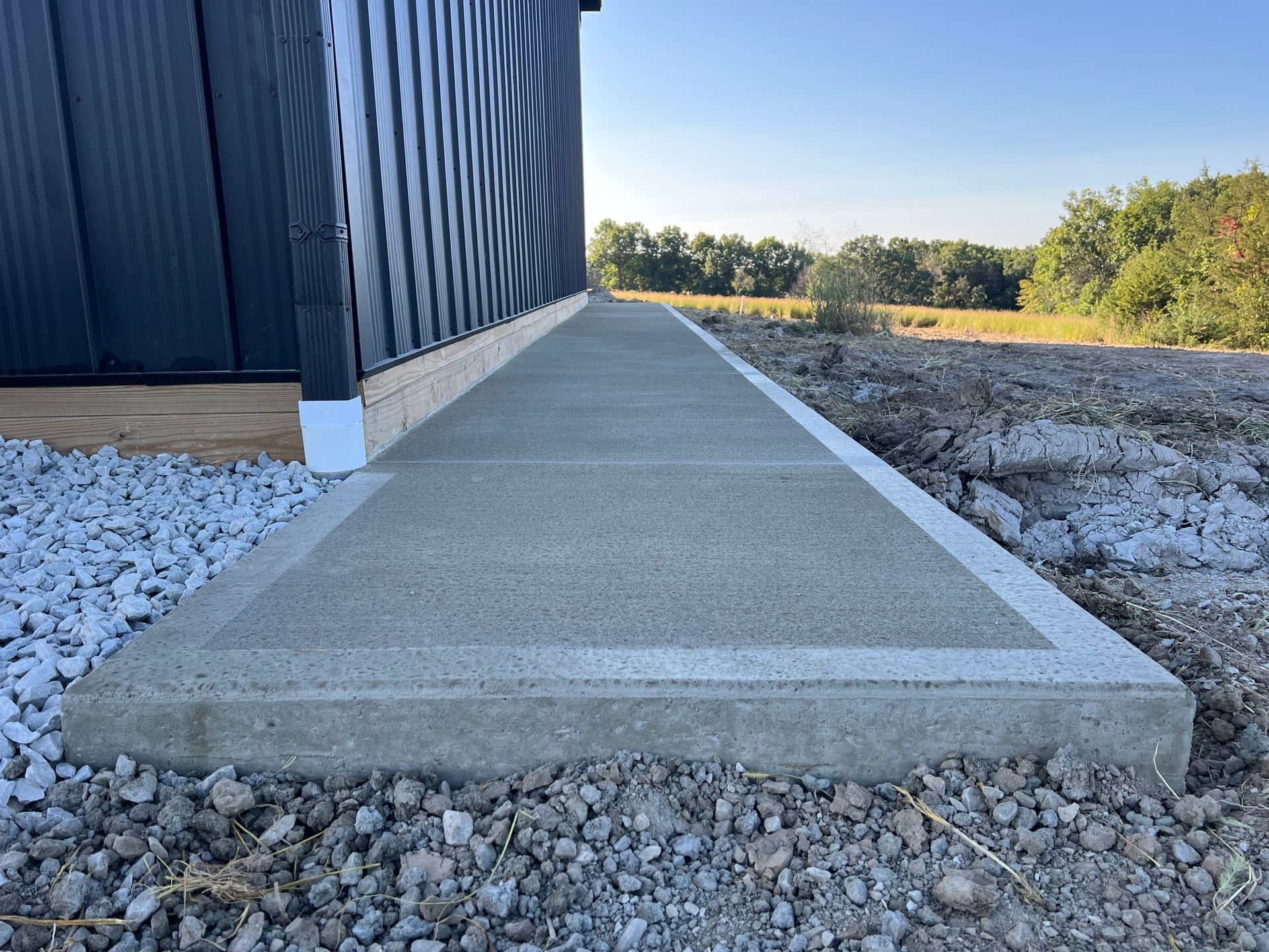 Concrete accessible walkway beside a blue building, bordered by gravel and a grassy field.