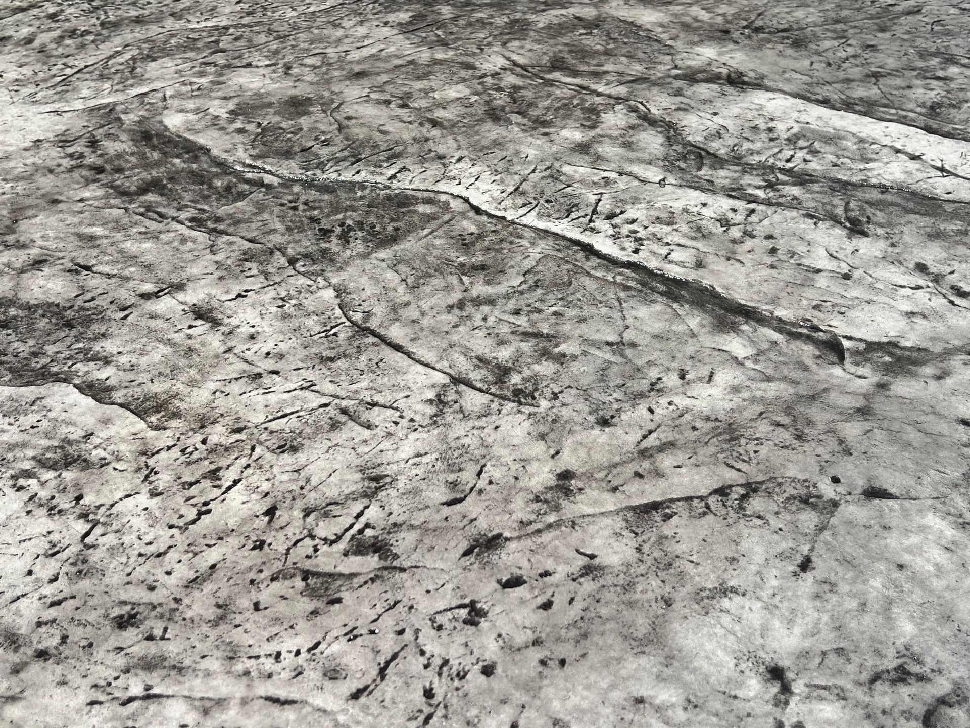 Close-up of weathered gray stone or concrete surface with cracks and dark speckled texture