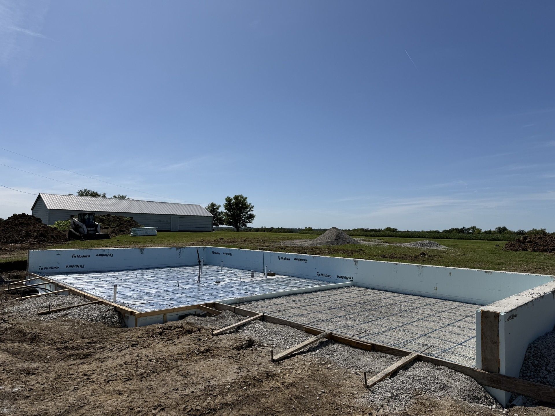 Partially built concrete foundation on a dirt lot under a clear blue sky
