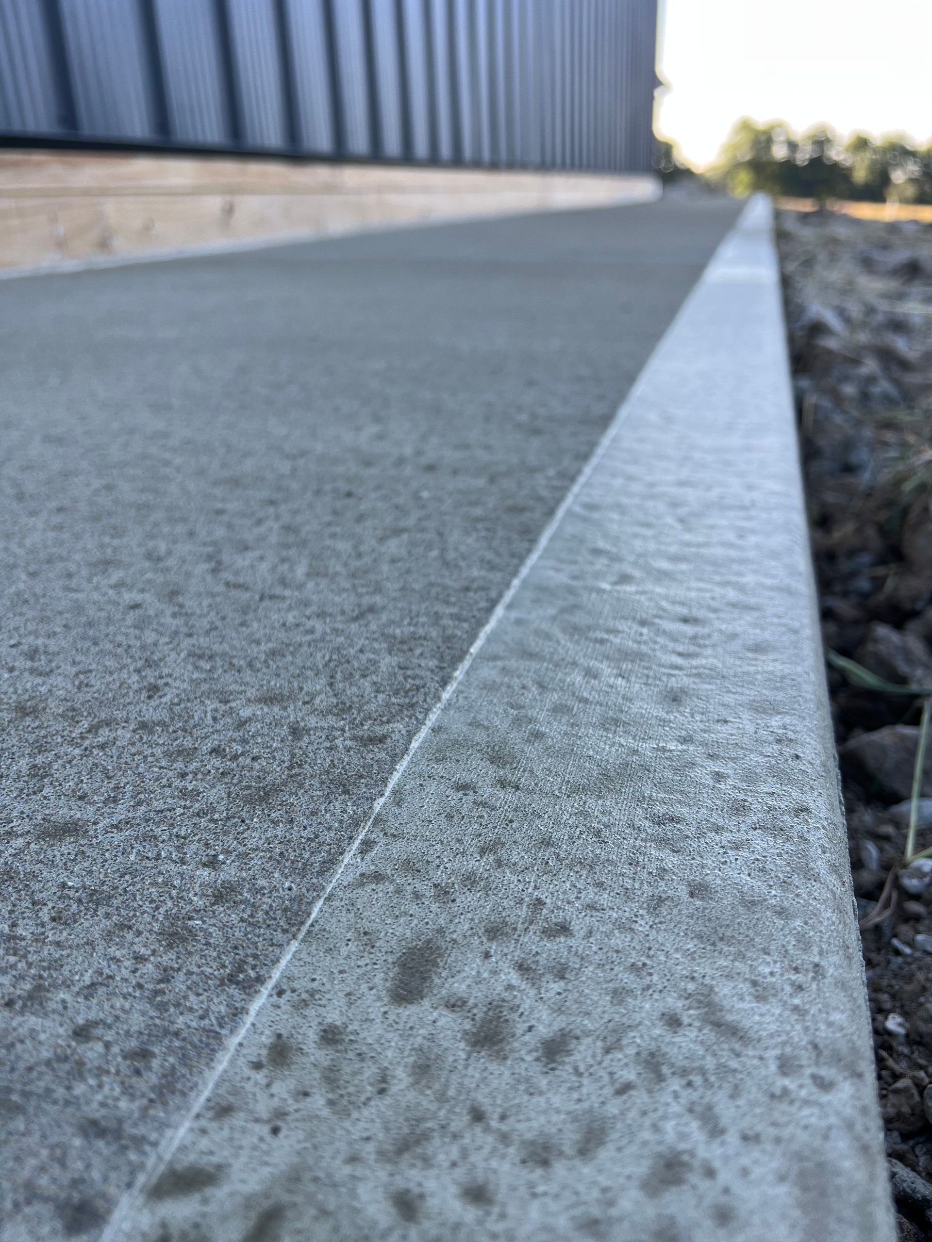 Concrete curb edge beside a building, with a gravel strip and blurred road in the background