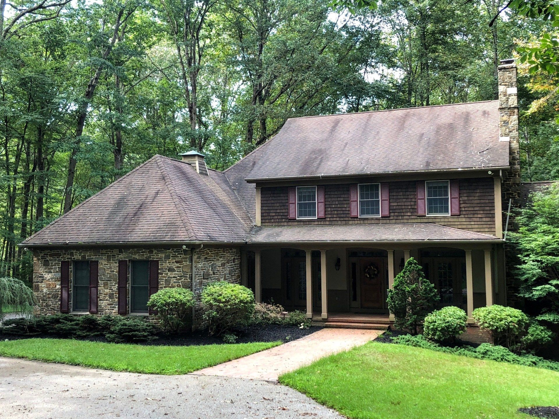 Suburban two-story brick house with a curved roof, front porch, and landscaped yard surrounded by trees