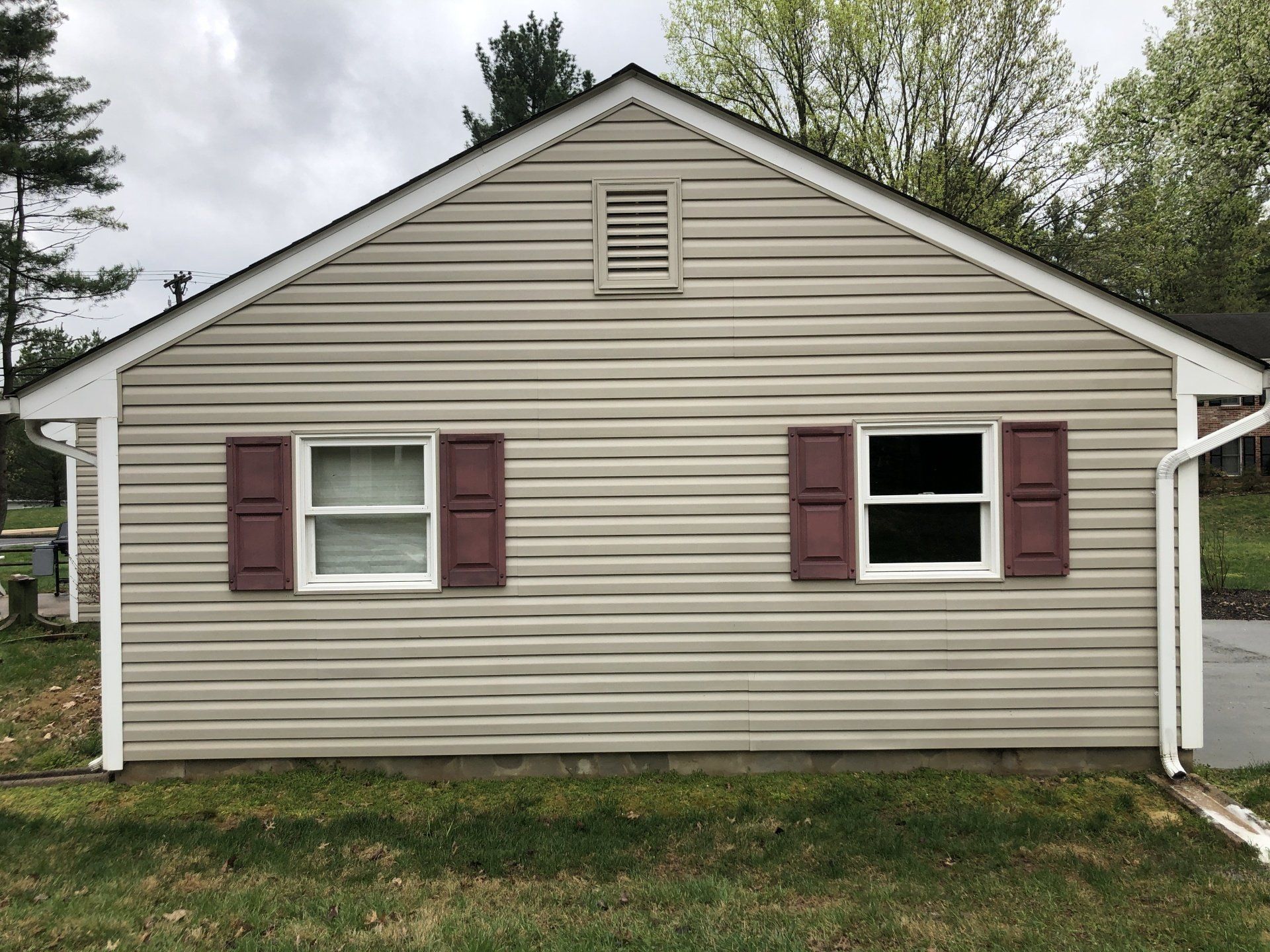 Single-story beige house exterior with maroon shutters, white trim, and a small attic vent.