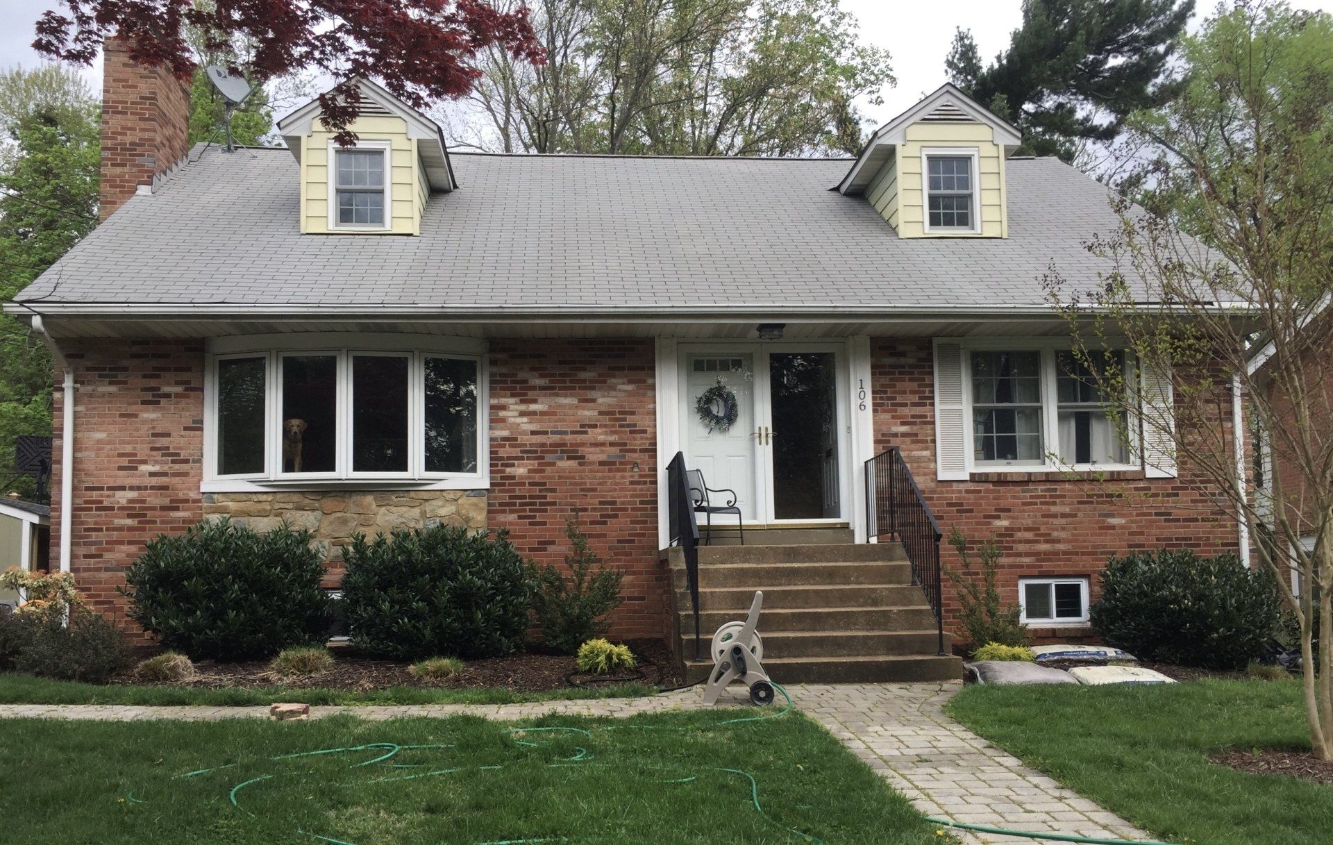 Brick house with white trim, front steps, and a small dog on the walkway under a gray roof.