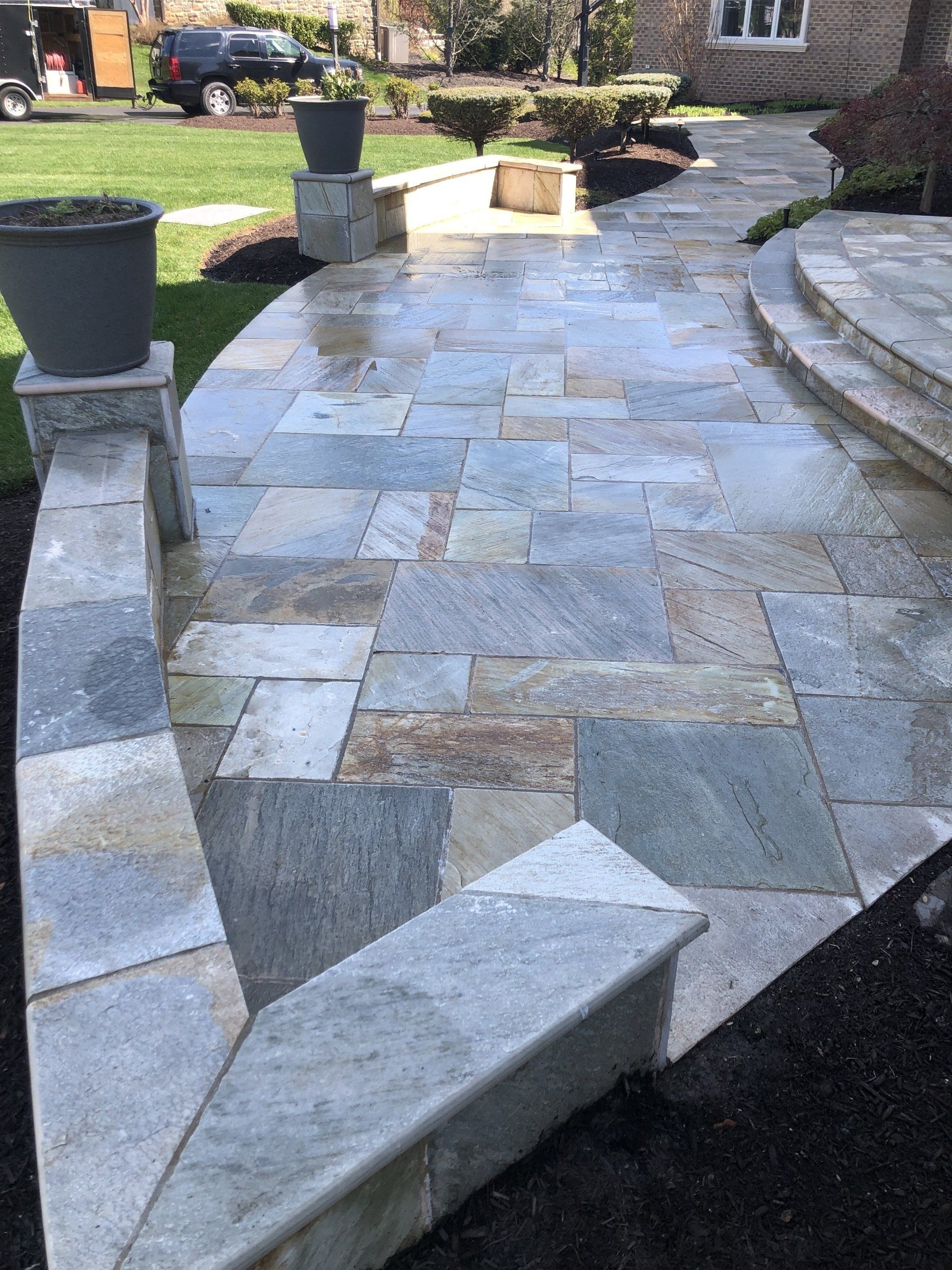 Stone-paved front walkway and steps with large planters in a landscaped yard