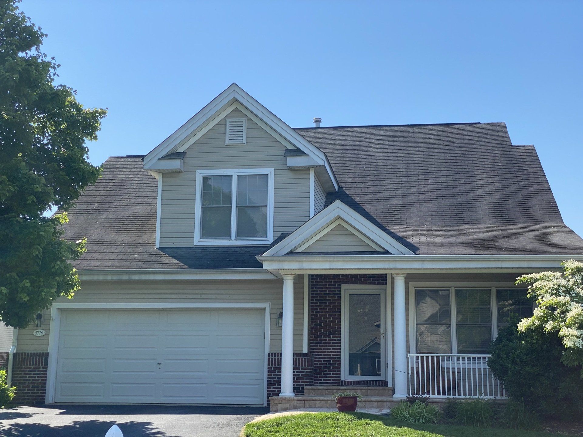 Suburban house with beige siding, gray roof, two-car garage, and a small front porch