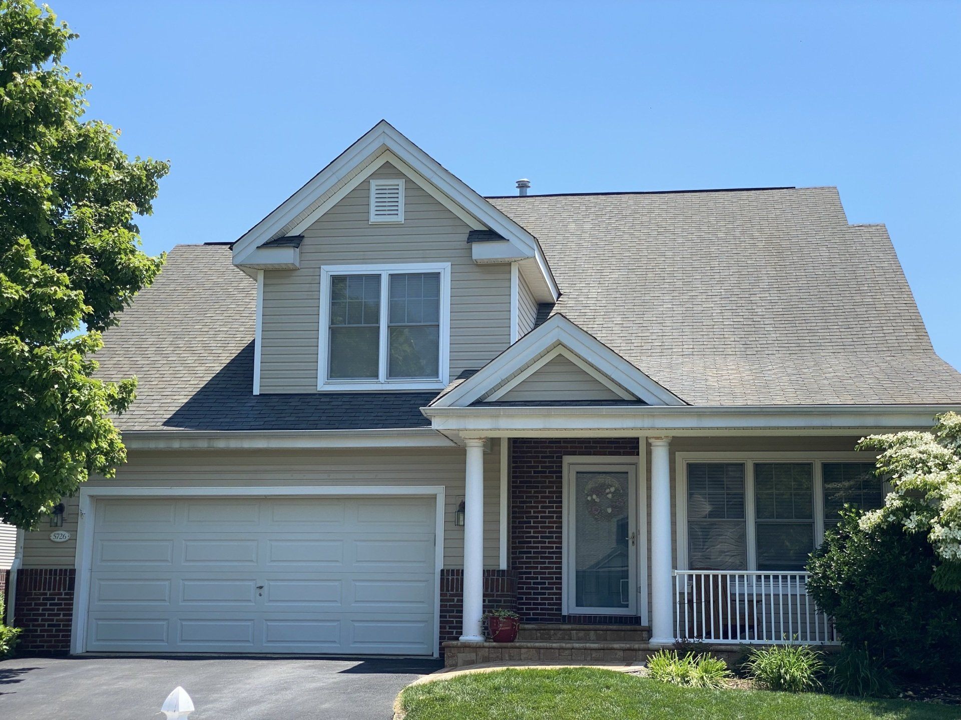 Two-story gray house with a white garage, gabled roof, and front porch on a sunny day