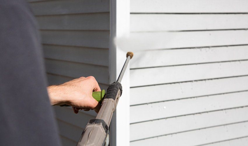 Person spraying the white siding of a house with a pressure washer