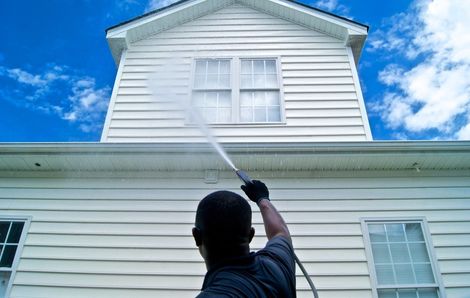 Person spraying water up the side of a white house against a blue sky