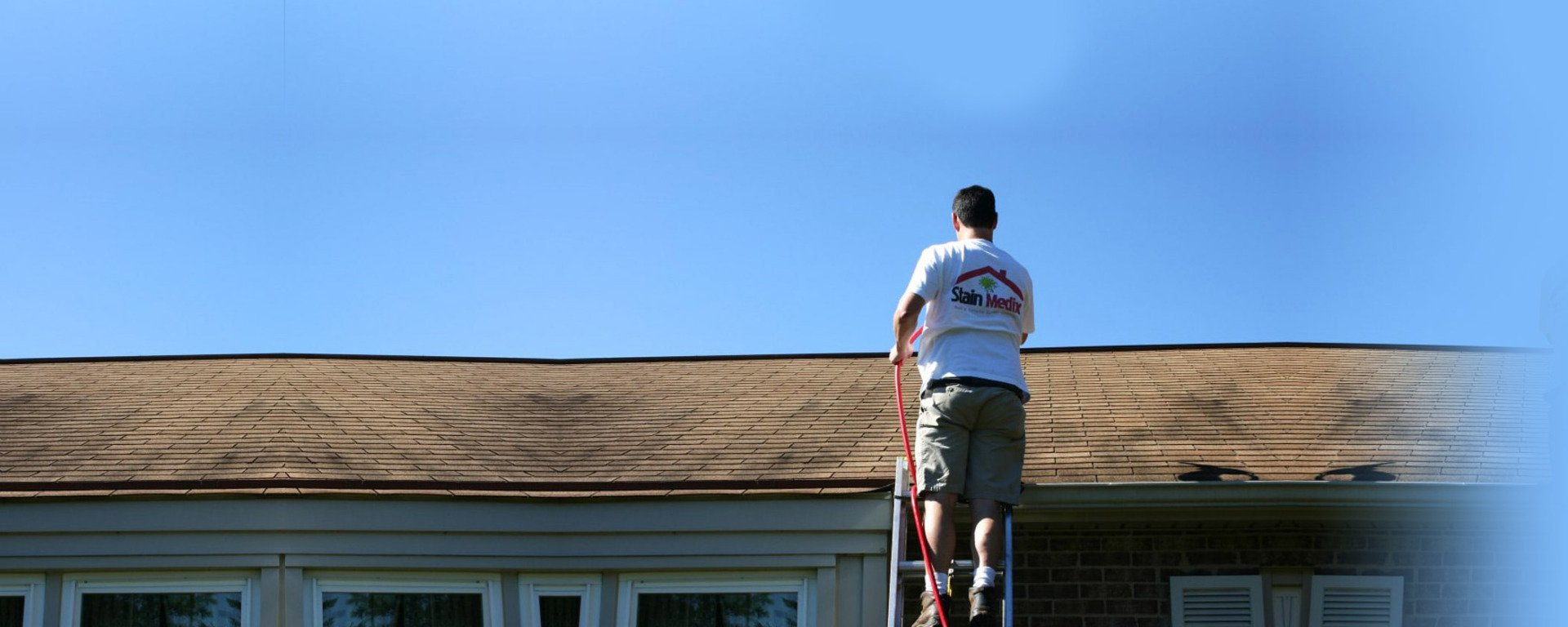 Person standing on a ladder on a roof under a blue sky