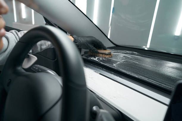 Person in black gloves cleaning a car dashboard with a brush; interior shot.