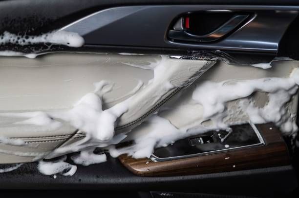 Car door interior covered in white soap, possibly during cleaning. Focus on panel detailing, wood trim, and handle.