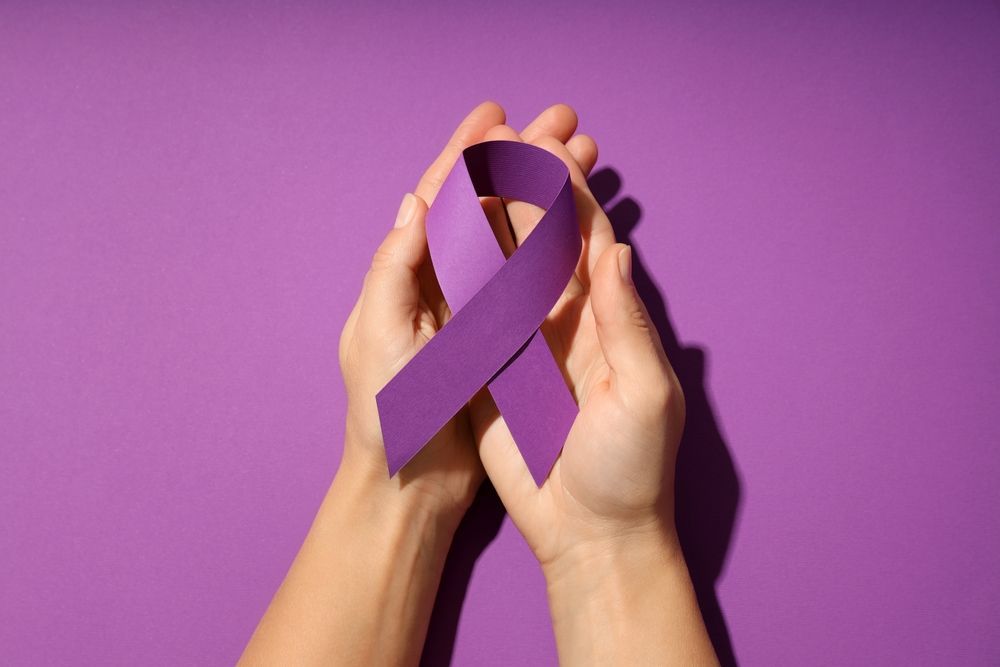 Hands holding a purple awareness ribbon against a purple background.