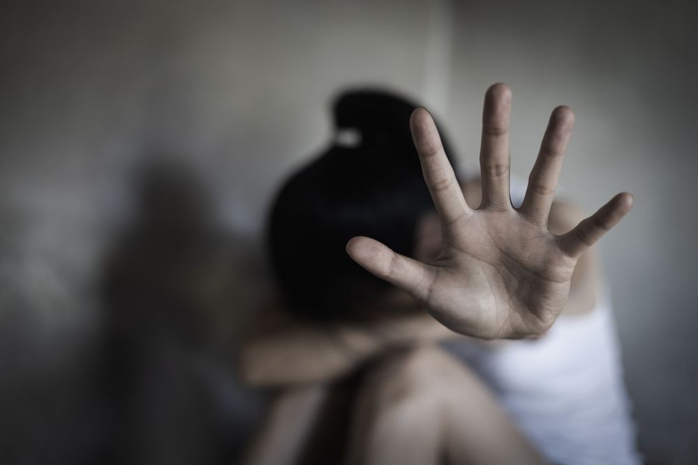 Person with raised open hand in foreground, blurred figure behind, suggesting distress or a stop gesture