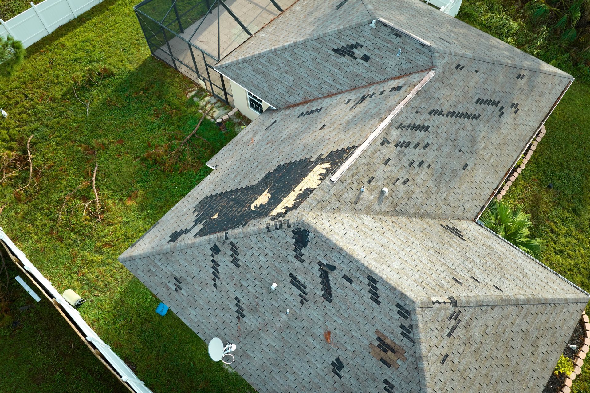 Aerial view of a gray-roofed house with solar panels beside a green lawn and driveway
