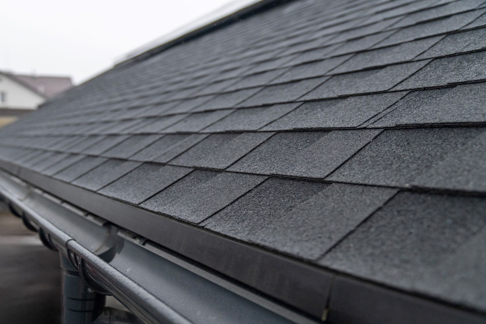 Dark asphalt shingle roof with a gray gutter, close-up shot.