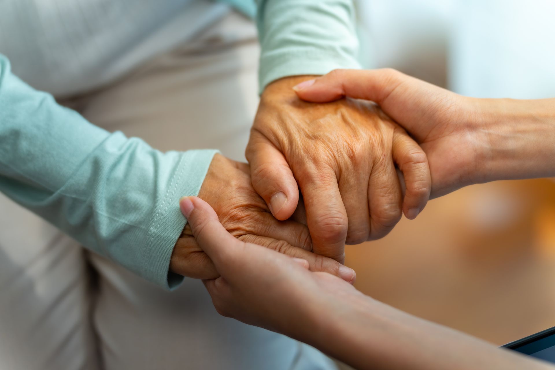 Hands of an older person being held by another person for support, light skin tones, soft colors.