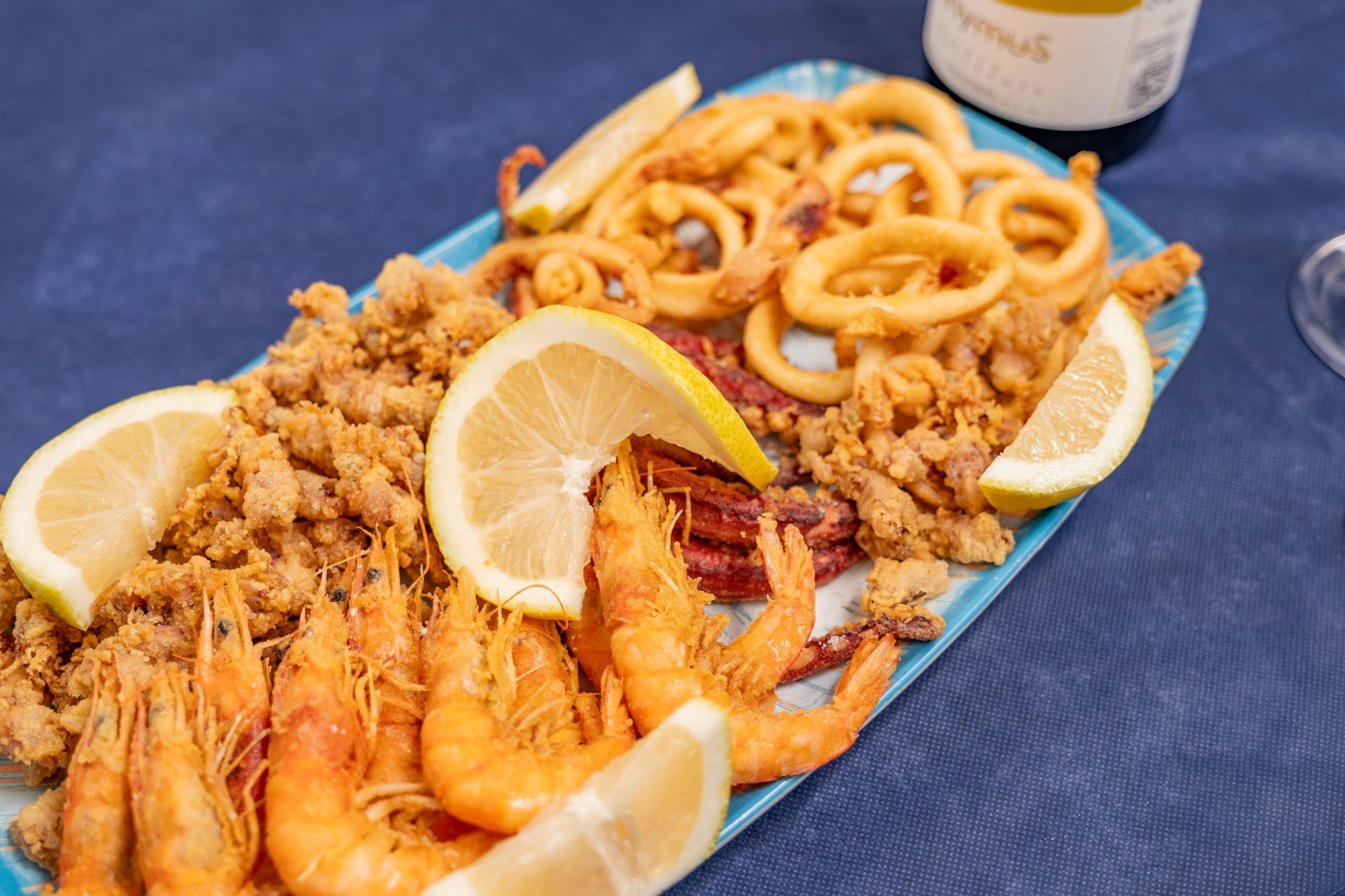 Piatto di frutti di mare fritti con spicchi di limone su un piatto blu, servito su una tovaglia blu.